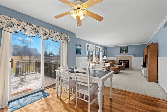 9009 N Pheasant Ridge Ln, Saline, MI 48176 - dining area with wainscoting, a fireplace, a ceiling fan, crown molding, and light wood-style flooring