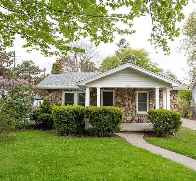 view of front of home featuring stone siding, a front lawn, a chimney, and covered porch