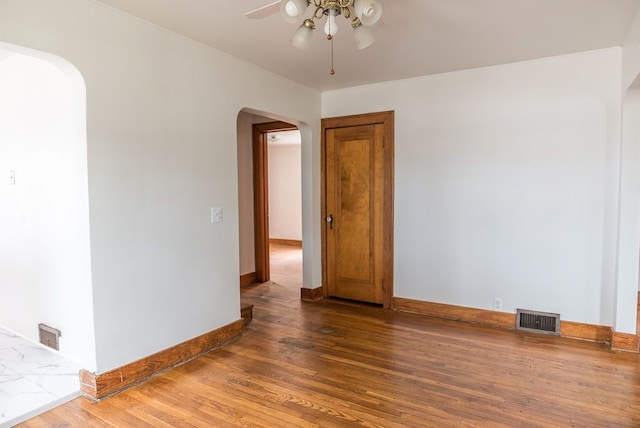 empty room featuring arched walkways, a ceiling fan, wood finished floors, and baseboards