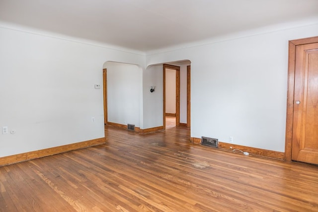 empty room with arched walkways, wood finished floors, and baseboards