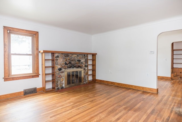unfurnished living room with wood finished floors, a stone fireplace, baseboards, and arched walkways