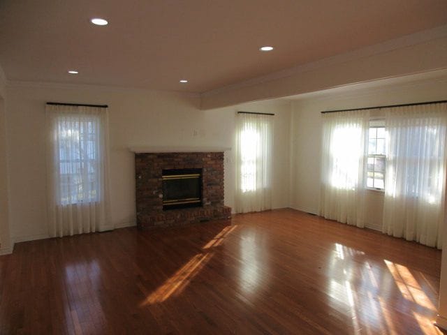 110 N 1st St, Holly, MI 48442 - unfurnished living room with plenty of natural light, wood finished floors, a brick fireplace, baseboards, and recessed lighting
