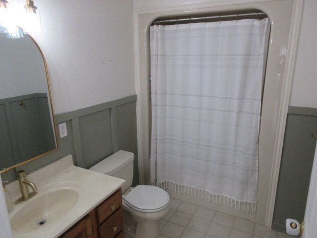 110 N 1st St, Holly, MI 48442 - full bath featuring a wainscoted wall, vanity, toilet, a decorative wall, and tile patterned floors