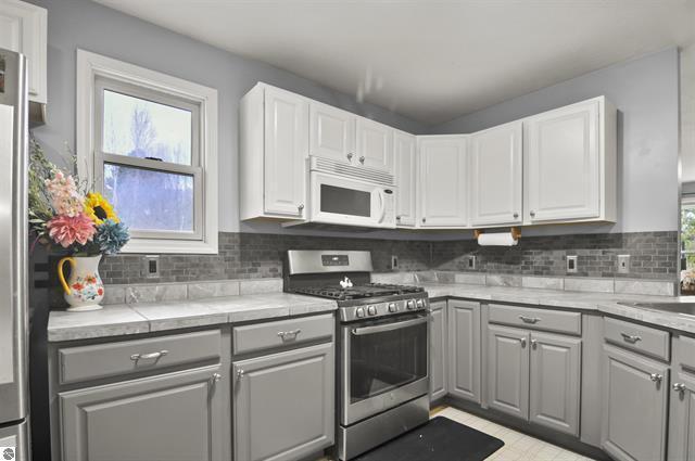 2426 E 48 1/2 Rd, Cadillac, MI 49601 - kitchen featuring stainless steel gas range, white microwave, gray cabinetry, and light countertops