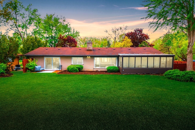 27607 Elba Dr, Grosse Ile, MI 48138 - back of house at dusk with a sunroom, a chimney, a patio area, and brick siding