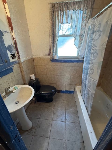 15779 Alden St, Detroit, MI 48238 - bathroom featuring tile walls, toilet, tile patterned floors, shower / bath combo, and a wainscoted wall