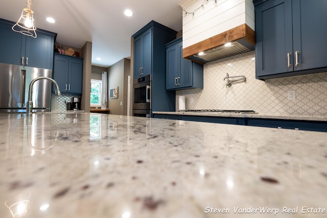 12640 Bucs Dr, Grand Haven, MI 49417 - kitchen with stainless steel appliances, custom range hood, blue cabinetry, tasteful backsplash, and recessed lighting