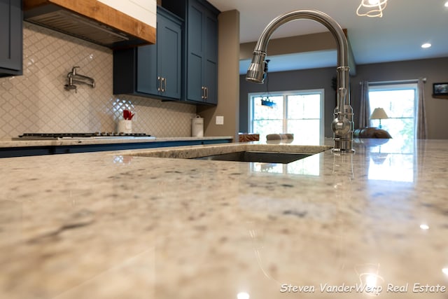 12640 Bucs Dr, Grand Haven, MI 49417 - kitchen with under cabinet range hood, backsplash, gas cooktop, light stone countertops, and recessed lighting