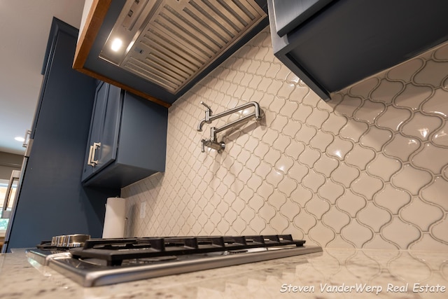 12640 Bucs Dr, Grand Haven, MI 49417 - kitchen with custom exhaust hood, tasteful backsplash, stainless steel gas stovetop, light stone countertops, and blue cabinets