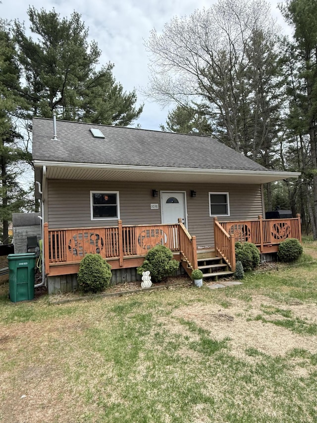 view of front of house with roof with shingles, a wooden deck, and a front yard