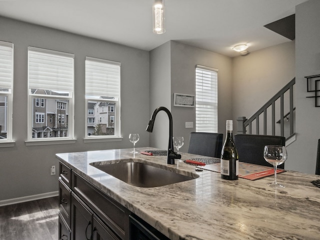 kitchen with a sink, wood finished floors, light stone countertops, and baseboards