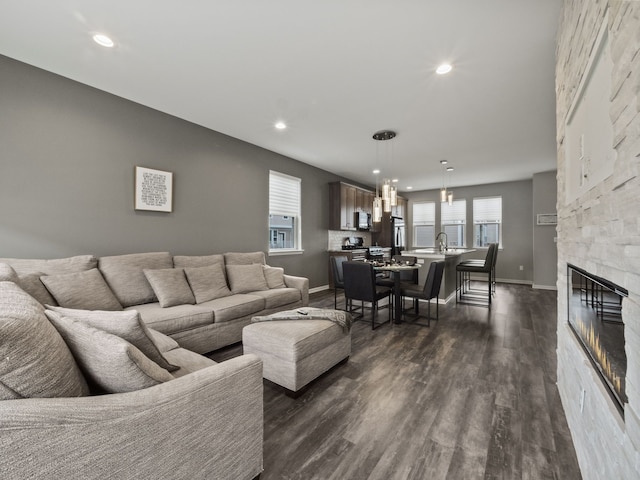 living area with recessed lighting, dark wood-type flooring, baseboards, and a stone fireplace