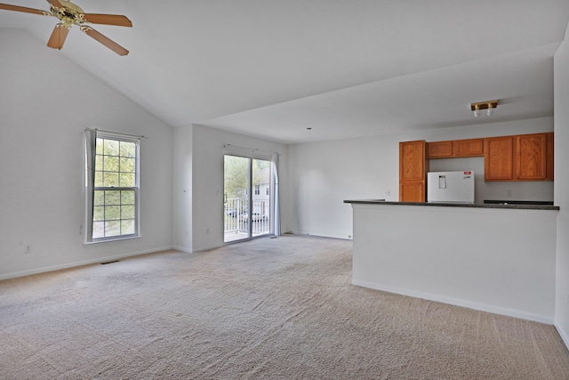 unfurnished living room with light colored carpet, healthy amount of natural light, ceiling fan, lofted ceiling, and baseboards