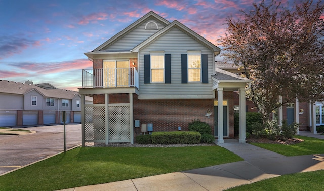 view of front facade featuring brick siding, a balcony, a lawn, and driveway