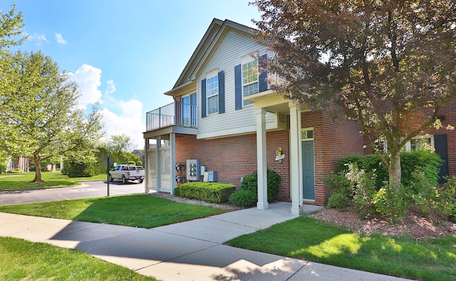 view of front of house with brick siding, a front yard, and a balcony