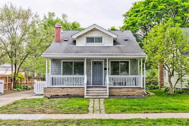 bungalow featuring covered porch, a chimney, and a shingled roof