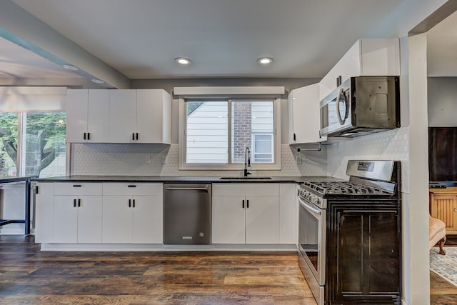 kitchen featuring stainless steel appliances, a sink, dark countertops, white cabinetry, and recessed lighting