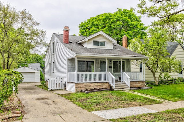 bungalow-style house with a chimney, covered porch, a garage, an outbuilding, and a front yard
