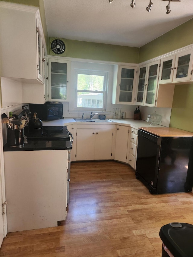 kitchen with a sink, black microwave, white cabinetry, light wood-type flooring, and fridge