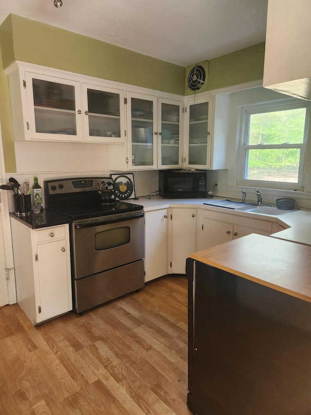 kitchen featuring stainless steel electric range oven, black microwave, light wood finished floors, and white cabinetry