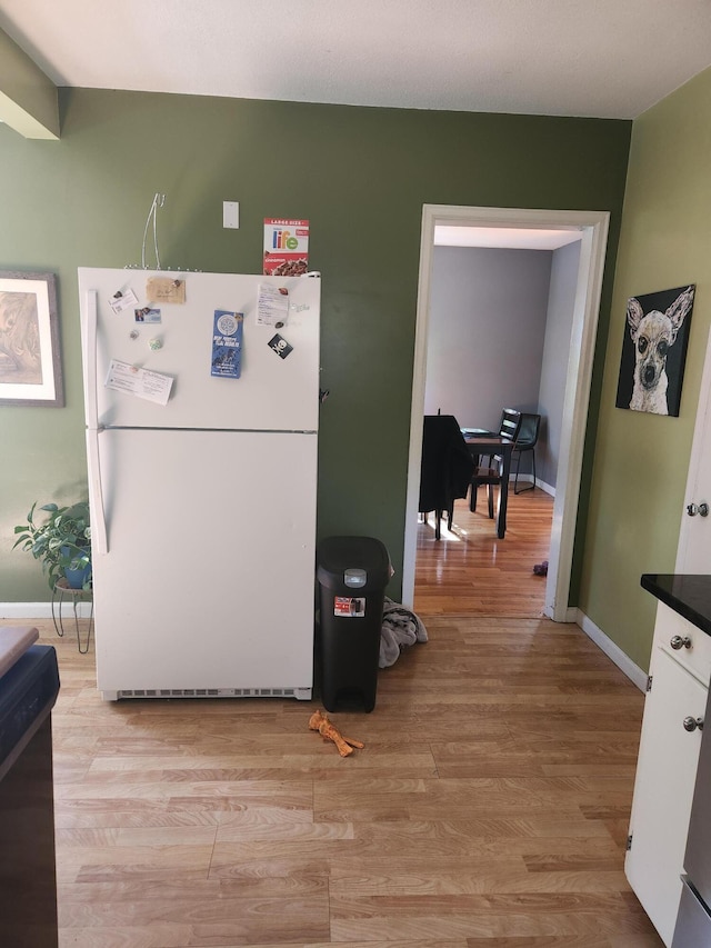 kitchen featuring freestanding refrigerator, white cabinets, light wood-style floors, and baseboards