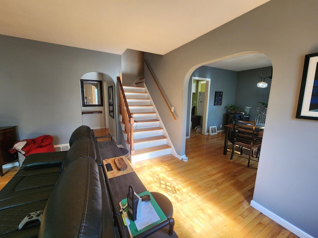 living room featuring arched walkways, light wood-style flooring, stairway, and baseboards