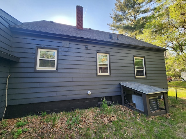 view of property exterior with a shingled roof, fence, and a chimney