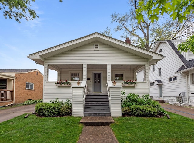 bungalow with covered porch, a front yard, and a chimney