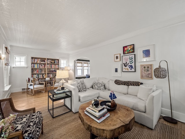 living room with arched walkways, light wood-style floors, ornamental molding, and baseboards
