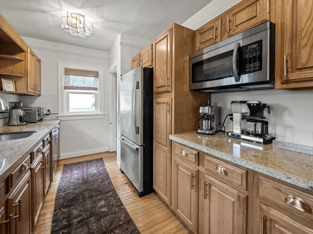 kitchen featuring stainless steel appliances, light wood finished floors, open shelves, and light stone countertops