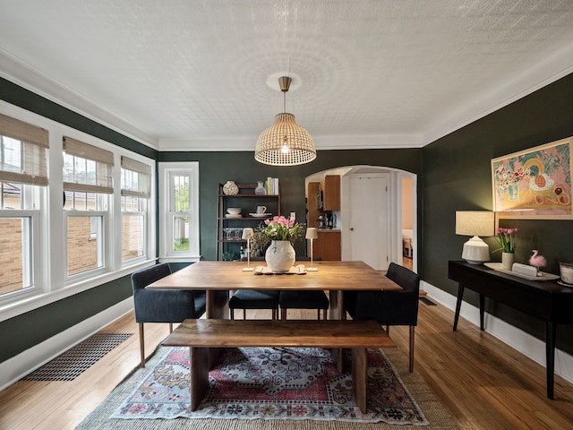 dining area with arched walkways, wood finished floors, crown molding, and baseboards