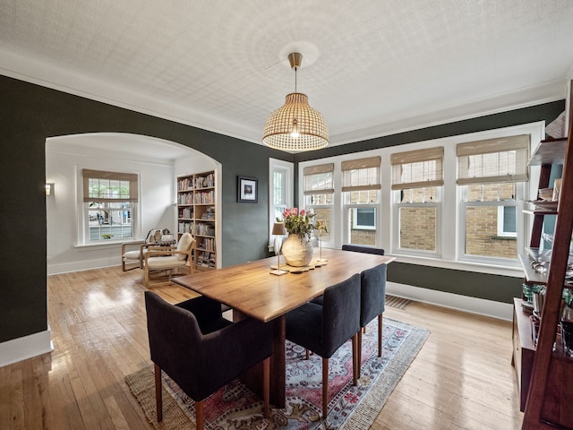 dining space featuring arched walkways, hardwood / wood-style floors, baseboards, ornamental molding, and built in features