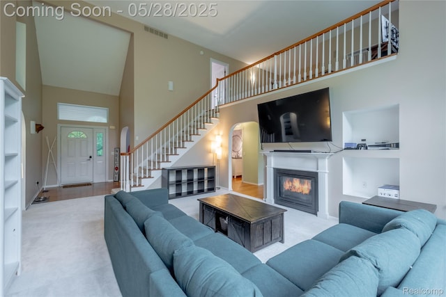105 Crescent Hill Dr, Ortonville, MI 48462 - living room featuring a towering ceiling, stairway, arched walkways, carpet floors, and a glass covered fireplace