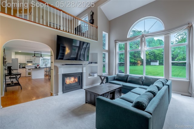 105 Crescent Hill Dr, Ortonville, MI 48462 - living area featuring high vaulted ceiling, light carpet, healthy amount of natural light, a glass covered fireplace, and arched walkways