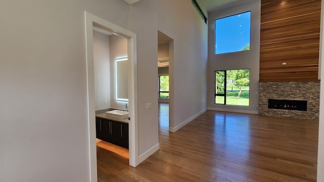 unfurnished living room with a sink, a towering ceiling, wood finished floors, a stone fireplace, and baseboards