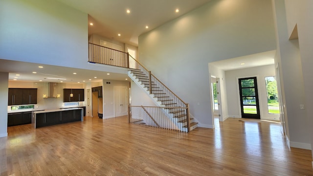 unfurnished living room with stairway, a towering ceiling, light wood-type flooring, recessed lighting, and baseboards