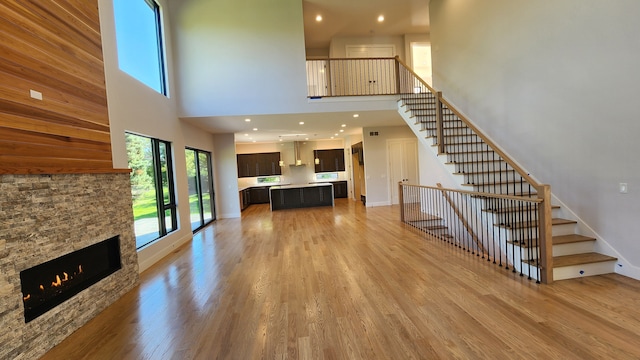 unfurnished living room featuring a high ceiling, stairs, light wood-type flooring, a stone fireplace, and recessed lighting