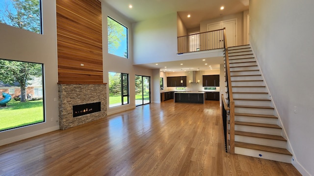unfurnished living room with a towering ceiling, stairway, a fireplace, light wood-type flooring, and recessed lighting