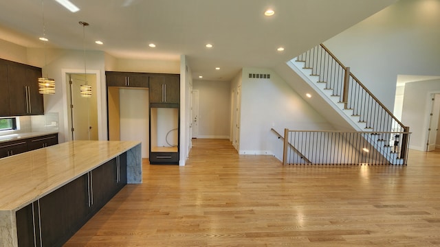 kitchen with dark brown cabinetry, light wood-type flooring, recessed lighting, light stone countertops, and baseboards