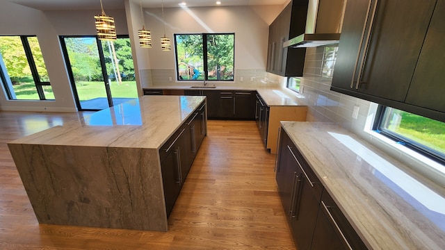 kitchen featuring light wood-style floors, a sink, light stone counters, wall chimney range hood, and healthy amount of natural light
