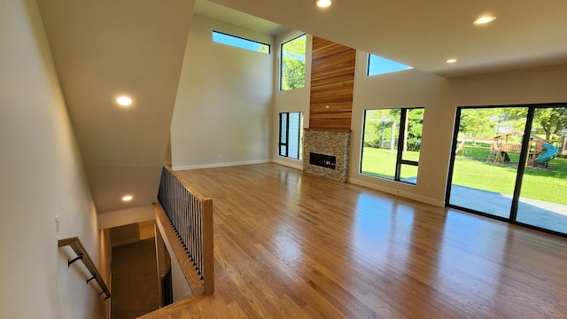unfurnished living room with recessed lighting, healthy amount of natural light, baseboards, wood finished floors, and a high ceiling