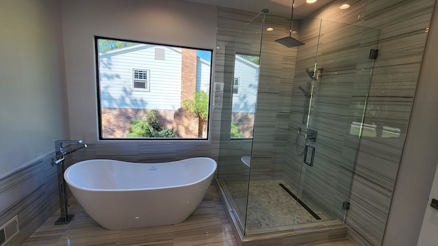 bathroom featuring plenty of natural light, a shower stall, a freestanding tub, tile walls, and wainscoting