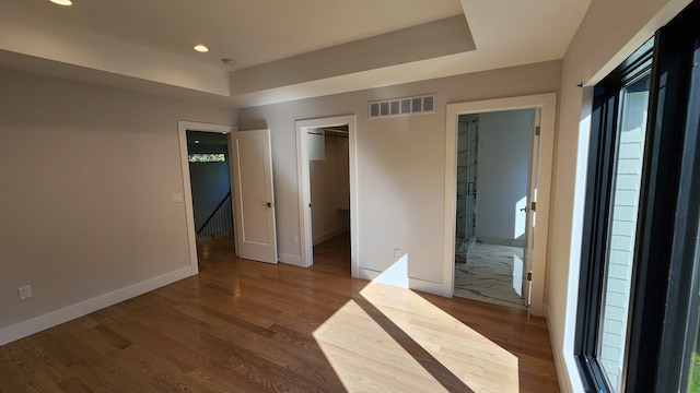 unfurnished bedroom with wood finished floors, recessed lighting, baseboards, a walk in closet, and a raised ceiling