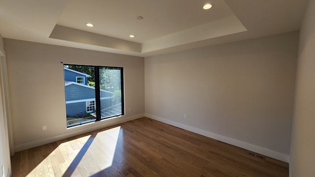 empty room with a tray ceiling, baseboards, wood finished floors, and recessed lighting