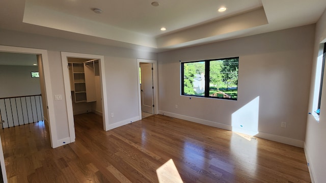 unfurnished bedroom with a raised ceiling, baseboards, a walk in closet, and recessed lighting