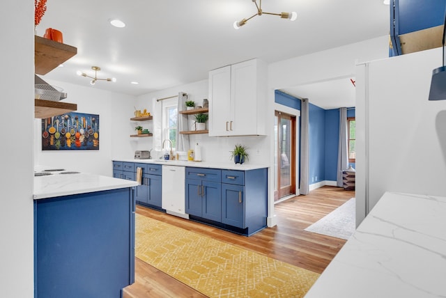 kitchen with open shelves, blue cabinets, white dishwasher, light wood-type flooring, and light stone countertops