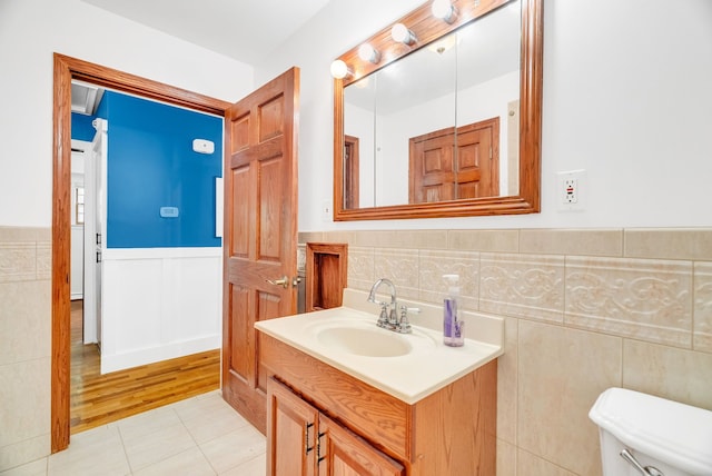 bathroom featuring toilet, a wainscoted wall, vanity, tile patterned flooring, and tile walls
