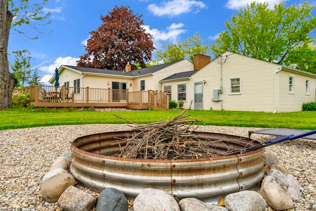 rear view of property with a deck, a yard, an outdoor fire pit, and a chimney