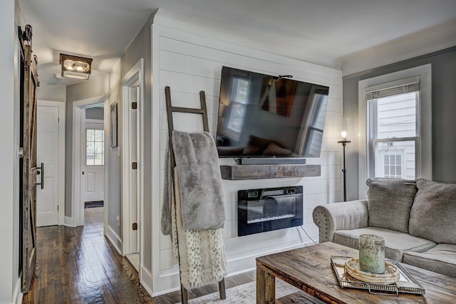 living area featuring dark wood-type flooring, a glass covered fireplace, and baseboards