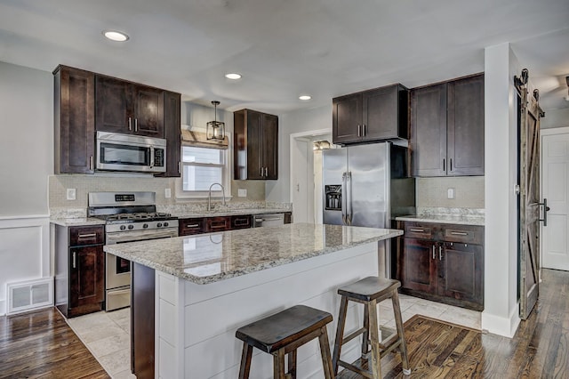 kitchen with appliances with stainless steel finishes, a sink, a kitchen bar, dark brown cabinets, and recessed lighting